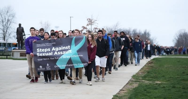 Students marching with a sign reading "Steps Against Sexual Assault"